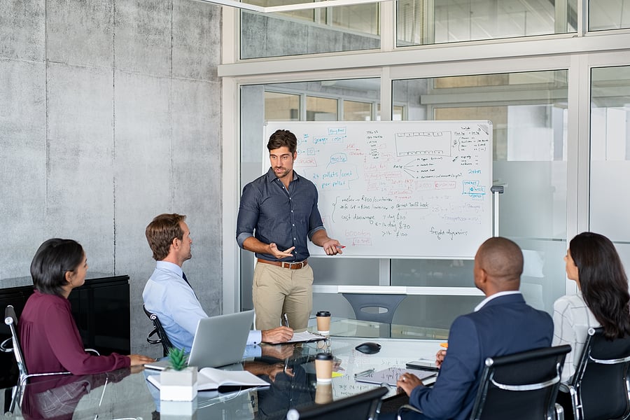 Executive presenting to colleagues at a whiteboard in a meeting