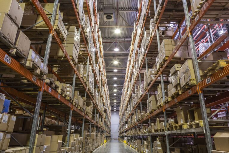 Long aisle of a distribution warehouse lined with stocked shelves