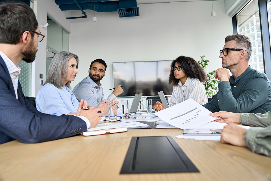 Five colleagues discussing documents around a boardroom table