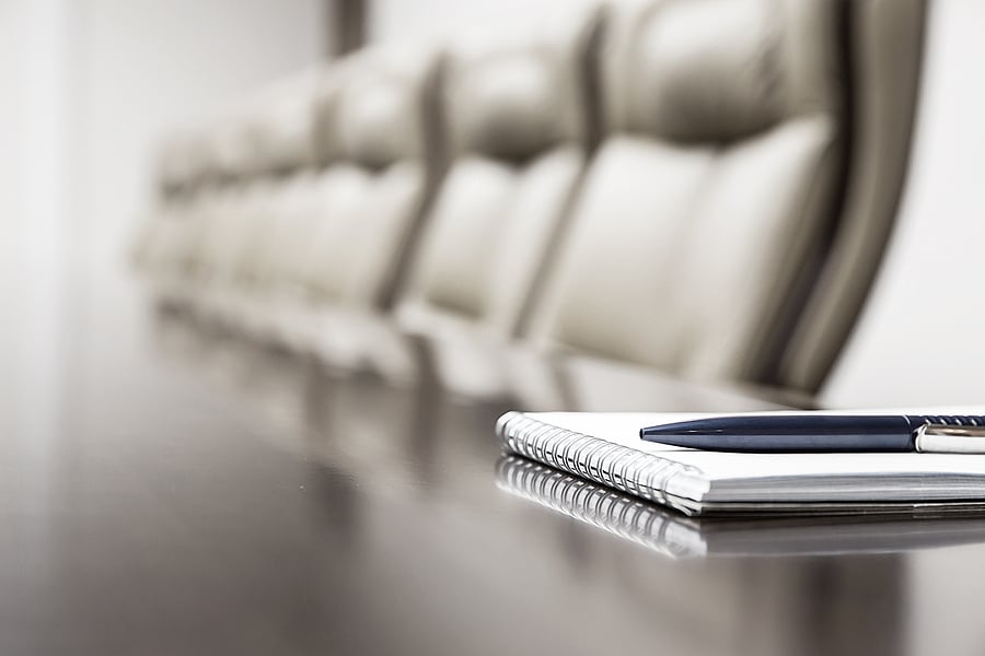 Notepad and pen on a boardroom table lined with empty chairs