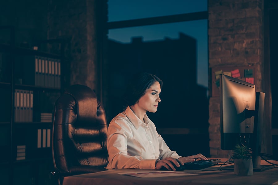 Woman working late at a computer in a dim office