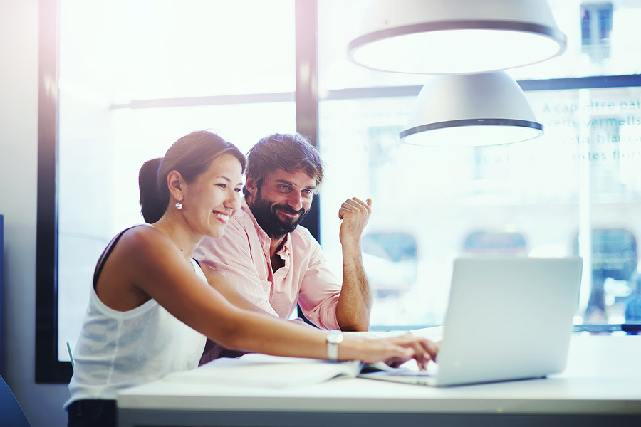Two colleagues smiling while looking at a laptop screen